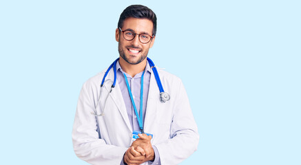 Young hispanic man wearing doctor uniform and stethoscope with hands together and crossed fingers smiling relaxed and cheerful. success and optimistic