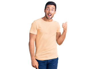 Young hispanic man wearing casual clothes smiling with happy face looking and pointing to the side with thumb up.