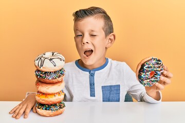Adorable caucasian kid eating doughnuts for breakfast winking looking at the camera with sexy...