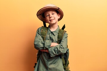 Cute blond kid wearing explorer hat and backpack happy face smiling with crossed arms looking at...