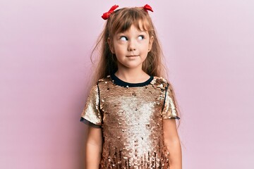 Little caucasian girl kid wearing festive sequins dress smiling looking to the side and staring away thinking.