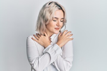 Young blonde girl wearing casual clothes hugging oneself happy and positive, smiling confident. self love and self care