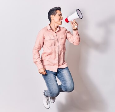 Young beautiful caucasian woman screaming using megaphone. Jumping over isolated white background