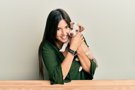 Young hispanic girl smiling happy and hugging dog sitting on the table over isolated white background.