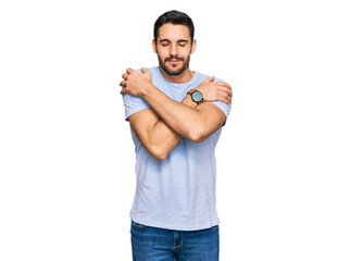 Young hispanic man wearing casual clothes hugging oneself happy and positive, smiling confident....