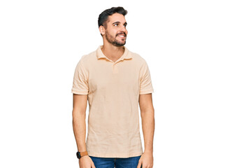 Fototapeta premium Young hispanic man wearing casual clothes looking away to side with smile on face, natural expression. laughing confident.