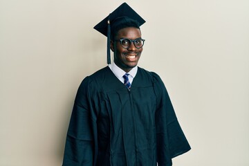 Handsome black man wearing graduation cap and ceremony robe with a happy and cool smile on face. lucky person.