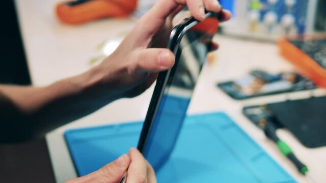 Repairman taking apart tablet body frame with pry opening tool