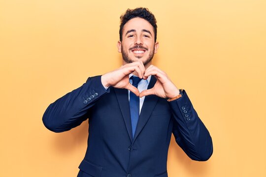 Young hispanic man wearing suit smiling in love doing heart symbol shape with hands. romantic concept.