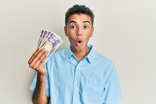 Young handsome african american man holding 5000 japanese yen banknotes scared and amazed with open mouth for surprise, disbelief face