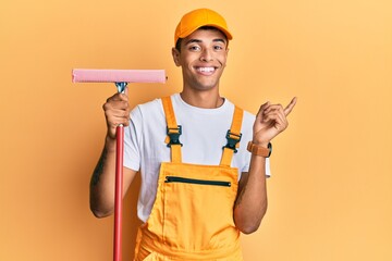 Young handsome african american man window cleaner holding glass washer smiling happy pointing with hand and finger to the side