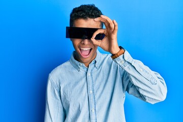 Young handsome african american man wearing banner glasses covering eyes smiling happy doing ok sign with hand on eye looking through fingers