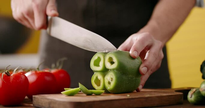 Close up shot of chef's hands using a knife cutting a fresh bell pepper on wooden board. Cooker preparing a vegetarian meal - food and drink 4k footage