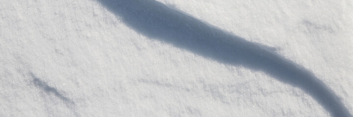 Beautiful winter background with snowy ground. Natural snow texture. Wind sculpted patterns on snow surface. Wide panoramic texture for background and design. Closeup top view with copy space.
