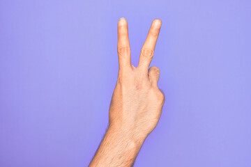 Hand of caucasian young man showing fingers over isolated purple background counting number 2 showing two fingers, gesturing victory and winner symbol