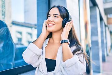 Young hispanic girl smiling happy listening to music using headphones at the city.