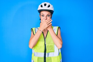 Young caucasian girl wearing bike helmet and reflective vest shocked covering mouth with hands for mistake. secret concept.