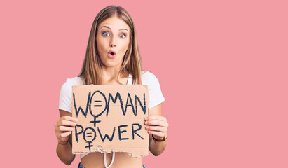 Young beautiful blonde woman holding woman power banner scared and amazed with open mouth for surprise, disbelief face