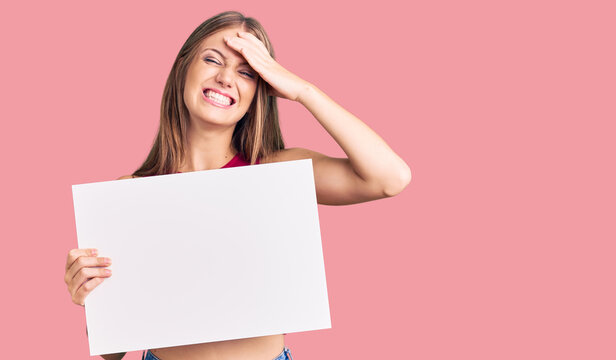 Young beautiful blonde woman holding blank empty banner stressed and frustrated with hand on head, surprised and angry face
