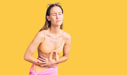 Obraz premium Beautiful brunette young woman wearing bikini and sunglasses with hand on stomach because indigestion, painful illness feeling unwell. ache concept.