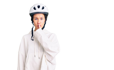 Beautiful brunette young woman wearing bike helmet and sporty clothes asking to be quiet with finger on lips. silence and secret concept.