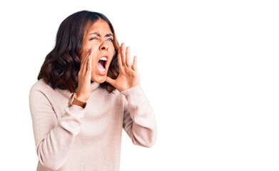 Young beautiful mixed race woman wearing winter turtleneck sweater shouting angry out loud with hands over mouth