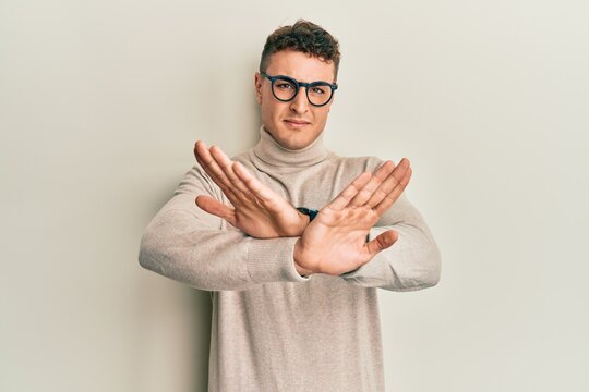 Hispanic young man wearing casual turtleneck sweater rejection expression crossing arms doing negative sign, angry face