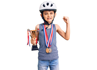 Little cute boy kid wearing bike helmet and winner medals holding winner trophy screaming proud, celebrating victory and success very excited with raised arms