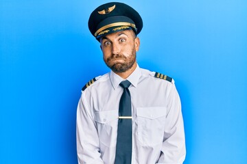 Handsome man with beard wearing airplane pilot uniform puffing cheeks with funny face. mouth inflated with air, crazy expression.