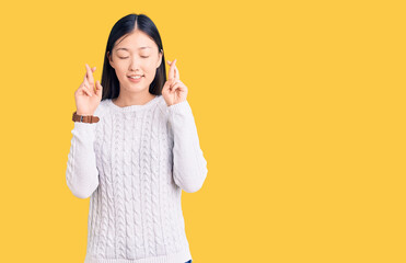 Young beautiful chinese woman wearing casual sweater gesturing finger crossed smiling with hope and eyes closed. luck and superstitious concept.