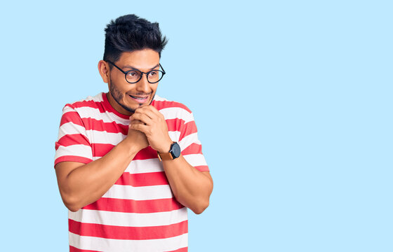 Handsome latin american young man wearing casual clothes and glasses laughing nervous and excited with hands on chin looking to the side