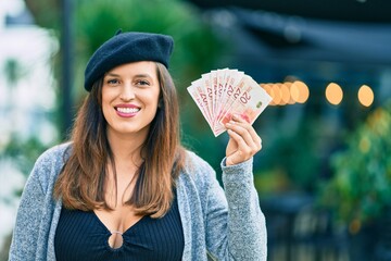 Young latin woman wearing french style holding israel shekels at the city.