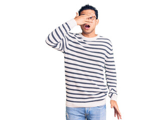 Fototapeta premium Hispanic handsome young man wearing casual clothes and glasses peeking in shock covering face and eyes with hand, looking through fingers with embarrassed expression.