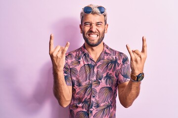Handsome blond man on vacation wearing casual shirt and sunglasses over pink background shouting...
