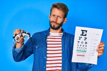 Handsome caucasian man with beard holding optometry glasses and eyesight test in shock face,...