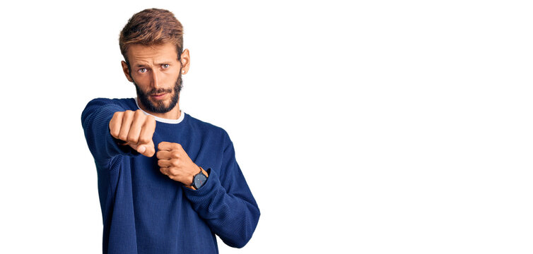 Handsome blond man with beard wearing casual sweater punching fist to fight, aggressive and angry attack, threat and violence