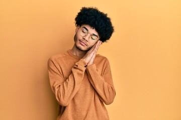Fototapeta na wymiar Young african american man with afro hair wearing casual winter sweater sleeping tired dreaming and posing with hands together while smiling with closed eyes.