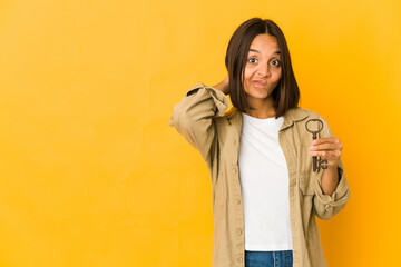 Young hispanic woman holding an old key touching back of head, thinking and making a choice.