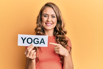 Fototapeta na wymiar Young blonde girl holding yoga message paper smiling happy pointing with hand and finger