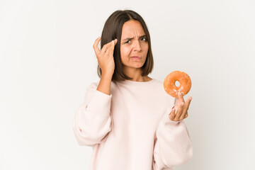 Young hispanic woman eating a doughnut pointing temple with finger, thinking, focused on a task.