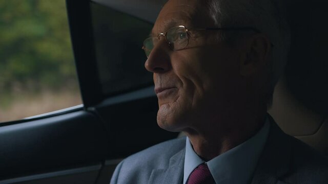 an elderly man in glasses and a suit rides in a car