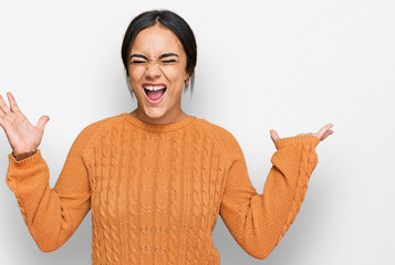 Young brunette woman wearing casual winter sweater celebrating mad and crazy for success with arms raised and closed eyes screaming excited. winner concept