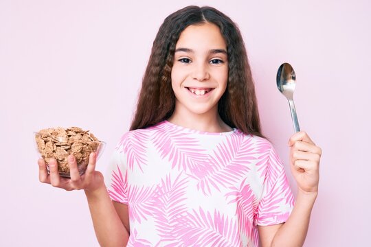 Cute hispanic girl holding cornflakes and spoon smiling with a happy and cool smile on face. showing teeth.