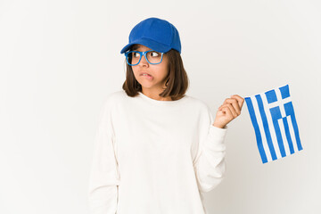 Young hispanic mixed race woman holding a greece flag confused, feels doubtful and unsure.
