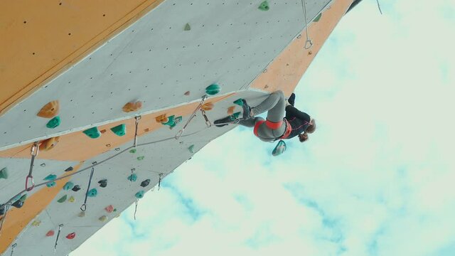 bottom view strong pretty girl climbing on overhanging rock wall on outdoor climbing center. woman making hard move on challenging route and falling. extreme sports, strength, training rockclimbing