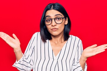 Young beautiful latin woman wearing casual clothes clueless and confused with open arms, no idea...