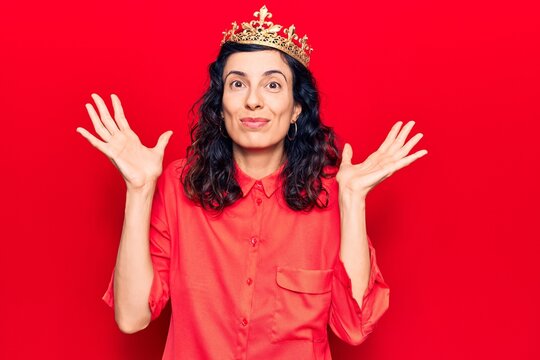 Young beautiful hispanic woman wearing princess crown clueless and confused with open arms, no idea and doubtful face.