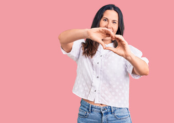 Young beautiful brunette woman wearing casual shirt smiling in love doing heart symbol shape with hands. romantic concept.
