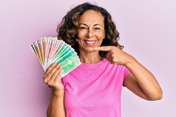 Middle age hispanic woman holding norwegian krone banknotes smiling happy pointing with hand and...