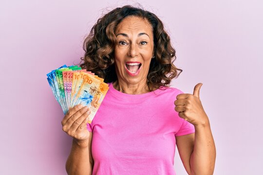 Middle age hispanic woman holding swiss franc banknotes pointing thumb up to the side smiling happy with open mouth